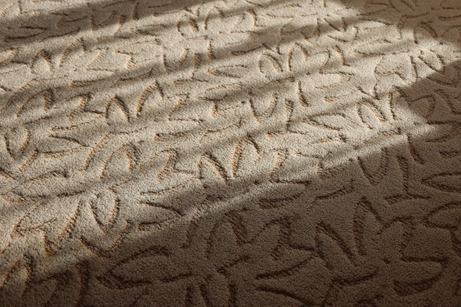 Close-up view of a beige carpet in a residential room, with visible marbled and handwritten-style markings etched into the surface, possibly indicating prior stain removal or cleaning markings. The carpet appears to be made of soft, synthetic fiber material, situated on a wooden floor, with even lighting from a nearby window casting subtle shadows. Part of the room is visible, showing a tidy environment with minimal furniture, and the area looks clean and well-maintained, suggesting professional cleaning or stain treatment conducted by [COMPANY_NAME]. The scene emphasizes surface cleaning and maintenance, aligning with deep cleaning and sanitisation services for residential spaces, as featured on the 'Emergency carpet stain removal Hampstead Heath local teams, WEST HAMPSTEAD' page.