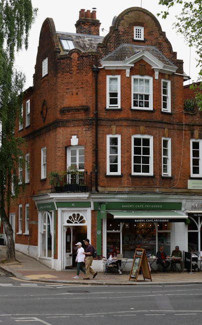 Two professional window cleaners from [COMPANY_NAME] are performing high-rise facade cleaning on a modern office building in West Hampstead. They are suspended from ropes, wearing helmets and harnesse
