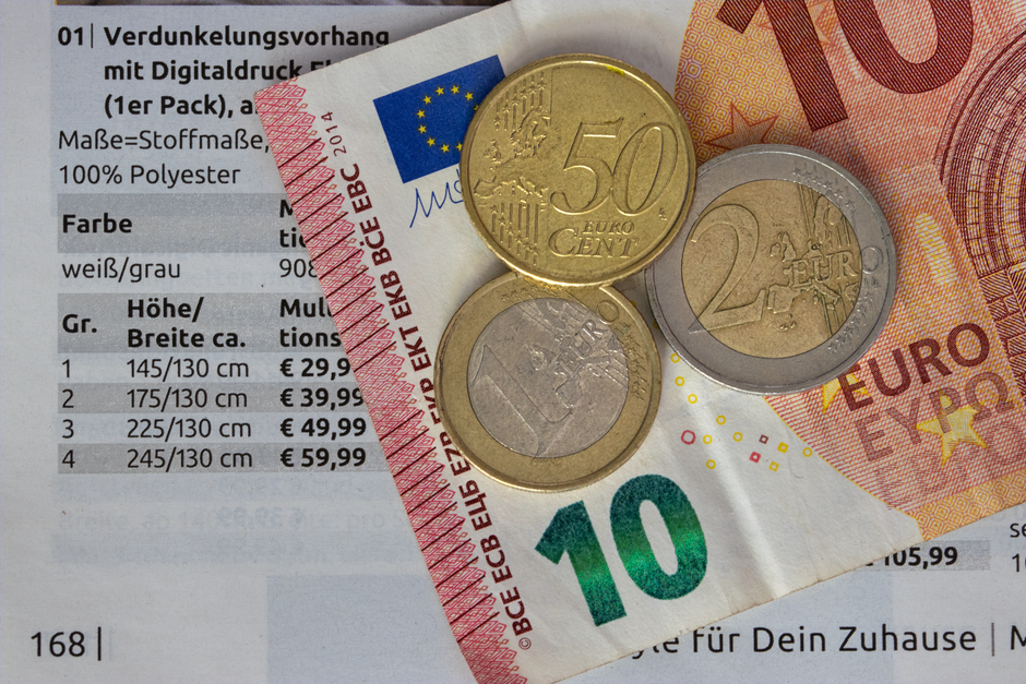 Close-up image showing a black calculator with blue and white buttons in the top left corner, positioned next to three neatly stacked piles of coins of various denominations, including copper and silv