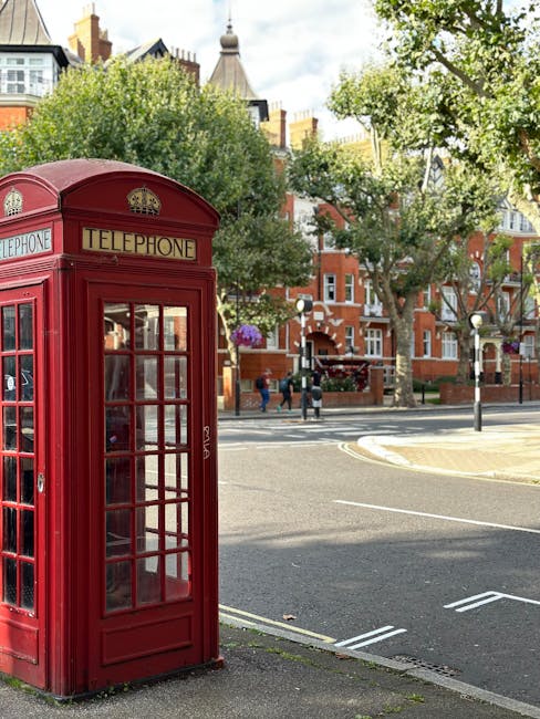 A red double-decker bus parked on a busy street in West Hampstead, London, with historic buildings lining the road and Tower of London in the background. The street features a combination of stone and brick surfaces, with parked cars and pedestrians visible. The scene is captured in natural daylight, with trees partially framing the image, showcasing the urban landscape of central London. This setting illustrates the need for surface cleaning and maintenance of urban environments, aligning with domestic and commercial cleaning services offered by [COMPANY_NAME] for properties in the West Hampstead NW6 area.